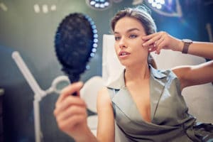 Young woman is looking her face in the mirror after a lip augmentation procedure