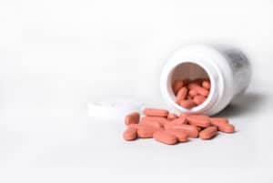 spilled pile of red tablets beside medicine bottle isolated on white